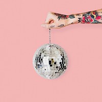 Tattooed hand holding Christmas glass ball with light pink background