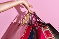 Woman carrying shopping bags against a pink background 