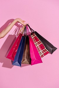 Woman carrying shopping bags against a pink background 
