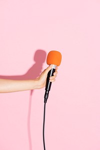 Hand holding a microphone with pink wall