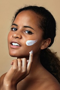 Beautiful African American woman using a moisturizing cream for skincare routine