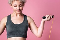 Young active girl with a skipping rope for cardio workout in a pink background studio