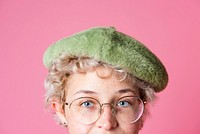 Studio portrait of a young girl wearing glasses and a greet beret in a pink background