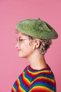 Side view of a cute girl wearing a rainbow sweater and a green beret in a pink background