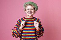 Studio portrait of a happy woman with rainbow sweater and glasses on a pink wall