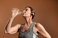 Thirsty senior woman in an active sportswear drinking water on a brown wall