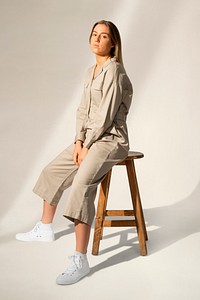 Sporty woman in beige jumpsuit sitting on a chair full body