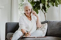 Senior businesswoman on a phone call writing on her planner at home