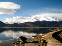 Vido al montego Kongur el la bordo de la Nigra Lago (Karakul), en Ĉinia Kirgizio; malfone ĉeborda tabulpaŝejo.. Original public domain image from Wikimedia Commons