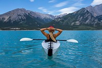 A woman wearing a hat and bracelets leaning back in a kayak in the very blue water in Nordegg. Original public domain image from Wikimedia Commons