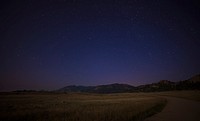 A country road with mountains in the distance under a starry night in Colorado.. Original public domain image from Wikimedia Commons