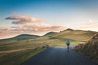 A cyclist riding on an empty road through countryside hills in the afternoon. Original public domain image from Wikimedia Commons