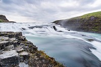 A low waterfall with foamy water flowing down between mossy rocks. Original public domain image from Wikimedia Commons