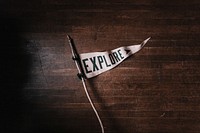 A white pennant that says explore on a dark wooden floor. Original public domain image from Wikimedia Commons