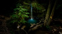 A high-angle shot of a waterfall pouring down a rocky ledge into a clear pond in the woods. Original public domain image from Wikimedia Commons