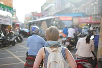 A short-haired woman with a backpack walking through a busy square. Original public domain image from Wikimedia Commons