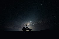 Silhouette of man standing on a car roof looking at the starry night sky with nebulas in Sossusvlei. Original public domain image from Wikimedia Commons