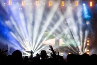 A shot from the back of the audience of a stage with tall beams of light and smoke. Original public domain image from Wikimedia Commons