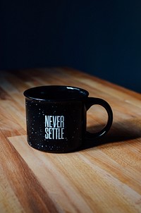 A black enamel mug with a “never settle” print. Original public domain image from Wikimedia Commons