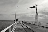 Black and white shot of pier boardwalk with cloudy sky in background. Original public domain image from <a href="https://commons.wikimedia.org/wiki/File:Monochrome_pier_boardwalk_(Unsplash).jpg" target="_blank" rel="noopener noreferrer nofollow">Wikimedia Commons</a>