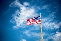 An American flag flying on a log pole against a blue sky with wispy clouds. Original public domain image from Wikimedia Commons
