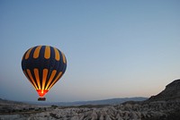 Hot air balloon floats over a mountain landscape at dusk. Original public domain image from Wikimedia Commons