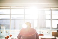 A man reading in an office directly sitting and facing towards the window flooded with rays of sunshine. Original public domain image from Wikimedia Commons