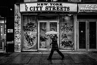 A black-and-white shot of a woman with an umbrella next to a dilapidated storefront. Original public domain image from <a href="https://commons.wikimedia.org/wiki/File:Monochrome_woman_umbrella_(Unsplash).jpg" target="_blank" rel="noopener noreferrer nofollow">Wikimedia Commons</a>
