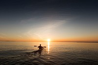 A man paddling in a kayak over the calm water in the evening during sunset. Original public domain image from Wikimedia Commons