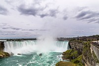 An impressive waterfall tumbling down from a rock face next to a town in Niagara Falls. Original public domain image from Wikimedia Commons