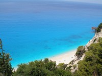 An empty sandy beach along an azure coast under rocky cliffs. Original public domain image from Wikimedia Commons