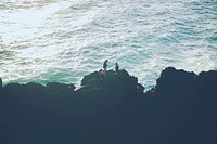Two people stood on the rocks at the most easterly point of the Australian mainland, with the sea beneath them. Original public domain image from Wikimedia Commons