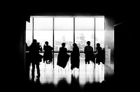 A black-and-white shot of people sitting on stools at a long table. Original public domain image from Wikimedia Commons