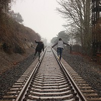 Two people balancing on the rails of a train track during a foggy day. Original public domain image from Wikimedia Commons