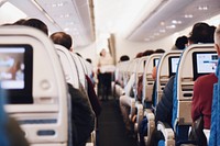 A view of the airplane aisle with a flight attendant carrying a tray. Original public domain image from Wikimedia Commons