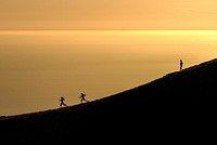 Three women energetically running down Mount Tamalpais as waters in the distance reflect the golden sunset. Original public domain image from Wikimedia Commons