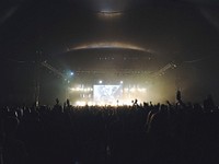 A shot from the back of a large concert audience with a large screen above the performing band. Original public domain image from <a href="https://commons.wikimedia.org/wiki/File:At_the_back_of_a_concert_venue_(Unsplash).jpg" target="_blank" rel="noopener noreferrer nofollow">Wikimedia Commons</a>