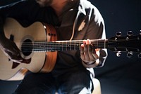 A seated person playing acoustic guitar. Original public domain image from Wikimedia Commons