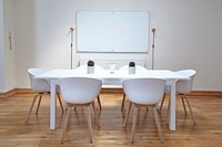 White chairs near a white table in a small conference room with a whiteboard. Original public domain image from Wikimedia Commons