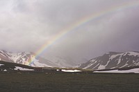 A landscape of rainbow over a field with a view of mountains covered in snow. Original public domain image from Wikimedia Commons