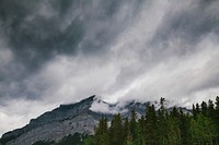 Clouds envelop a rugged mountain with a coniferous forest at its base. Original public domain image from Wikimedia Commons