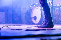 A low shot of a musician's jeans and shoes on a stage. Original public domain image from Wikimedia Commons