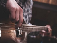 A bleak shot of a person in a checkered shirt strumming a guitar. Original public domain image from Wikimedia Commons