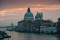 Light orange and pink sunset reflected in the water in Venice, with clear cityscape and architecture in detail.. Original public domain image from Wikimedia Commons