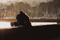 A couple sit on the harbour wall in Quai Gustave Doret, with boats in the background as the sun sets at dusk.. Original public domain image from <a href="https://commons.wikimedia.org/wiki/File:Spring_love_(Unsplash).jpg" target="_blank" rel="noopener noreferrer nofollow">Wikimedia Commons</a>