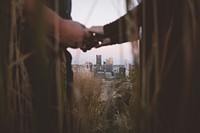 A couple is seen holding hands through tall grasses, with the Pittsburgh skyline in the background. Original public domain image from Wikimedia Commons