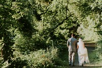 A bridal couple walking on a dirt path lined with trees. Original public domain image from <a href="https://commons.wikimedia.org/wiki/File:Bride_and_groom_walking_in_woods_(Unsplash).jpg" target="_blank" rel="noopener noreferrer nofollow">Wikimedia Commons</a>