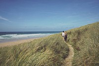 Two women walking on the path through the grass coastline in Perranporth, England, United Kingdom. Original public domain image from Wikimedia Commons