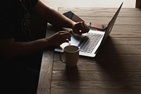 A man working on a laptop at a table with a mug and two iPhones. Original public domain image from <a href="https://commons.wikimedia.org/wiki/File:Mobile_developer_at_work_(Unsplash).jpg" target="_blank" rel="noopener noreferrer nofollow">Wikimedia Commons</a>