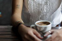 A woman with a “guts over fear” tattoo sitting over coffee. Original public domain image from <a href="https://commons.wikimedia.org/wiki/File:Guts_over_fear_(Unsplash).jpg" target="_blank" rel="noopener noreferrer nofollow">Wikimedia Commons</a>